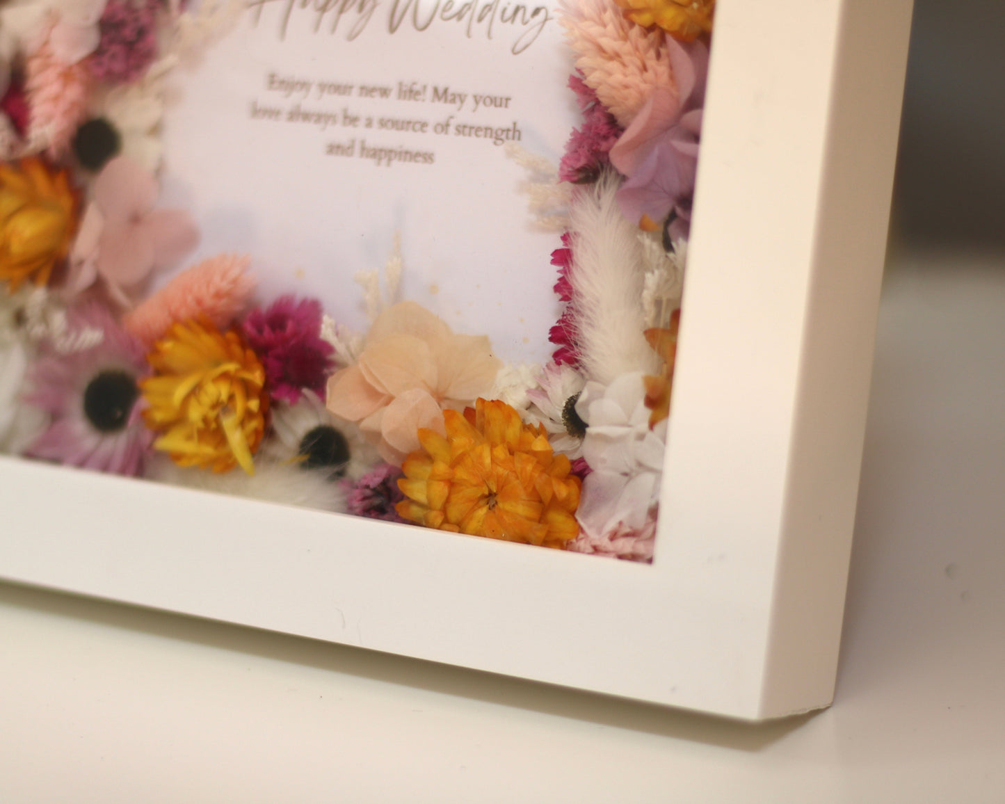 A lower corner of a picture frame decorated with orange, pink and white field flowers