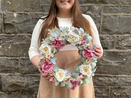 A wreaths form artificial white and pink flowers with pale green leaves in girls hands