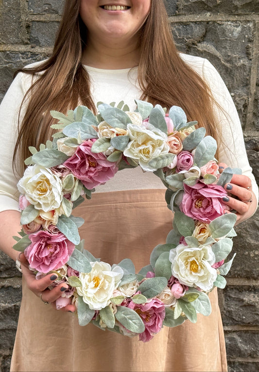 A wreaths form artificial white and pink flowers with pale green leaves in girls hands