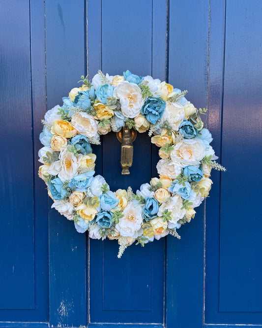 Yellow and blue artificial flowers in a beautiful floral wreath on a blue door