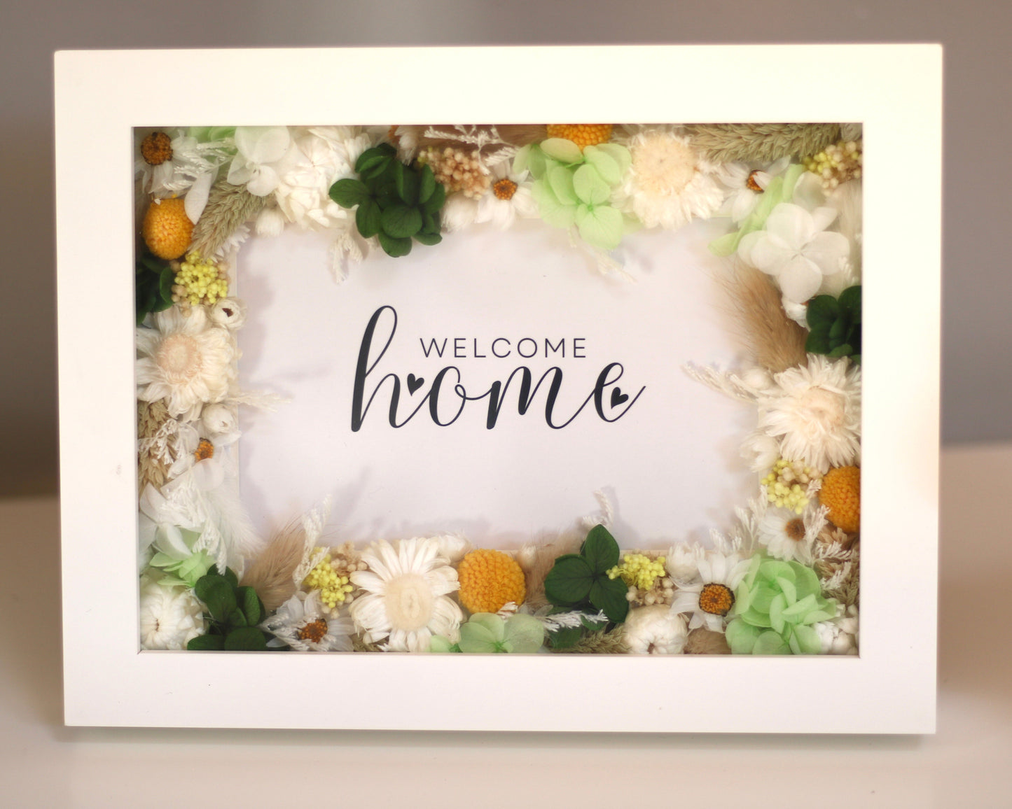 A white picture frame decorated with white field flowers and green foliage