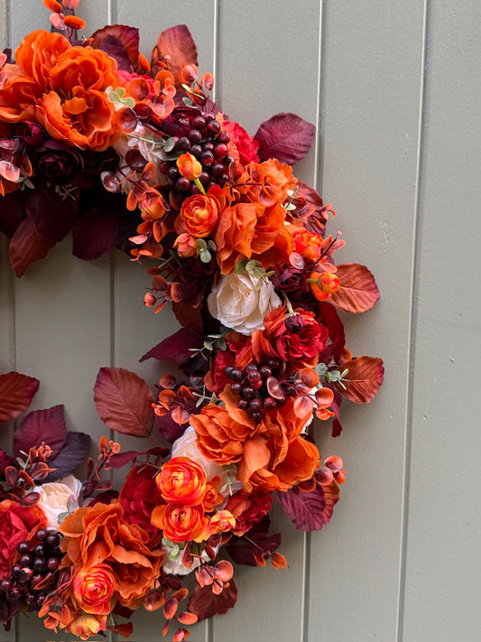 Autumn-themed floral wreath with orange, red, and purple flowers on a gray door.