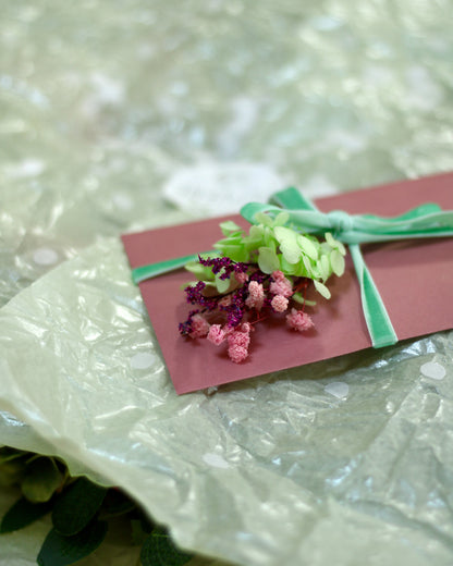 A congratulations card with a green velvet bow decorated with flowers on a light-green wrapping paper