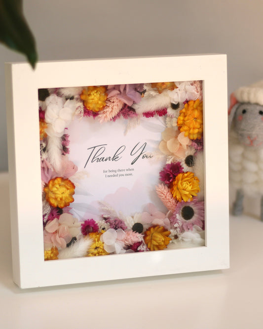 A thank you note in a rectangular picture frame decorated with pink, white and white flowers 