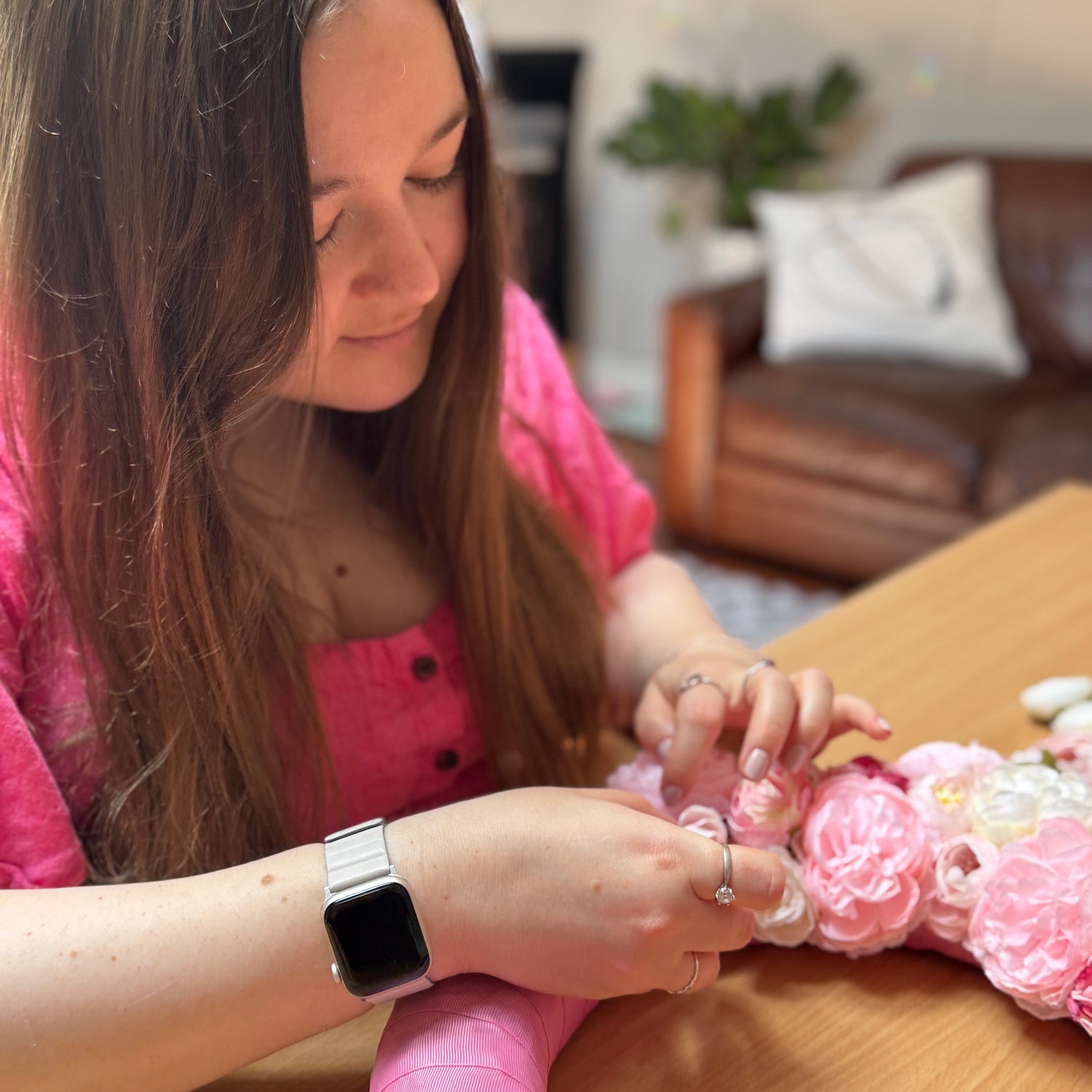 A woman in pink dress creates a decorative floral wreath